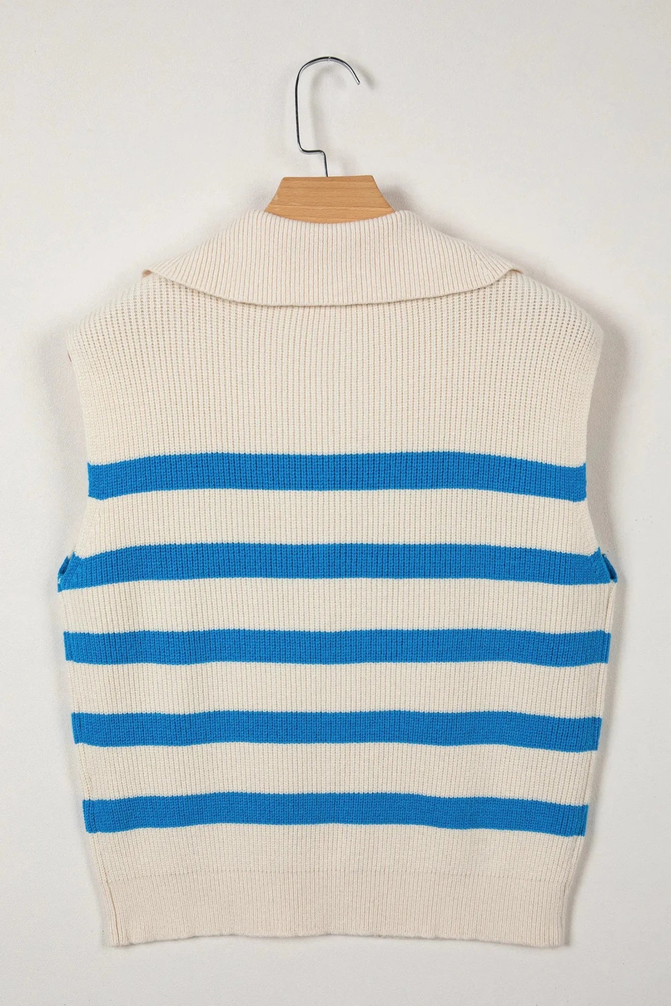A sleeveless ribbed knit sweater vest in cream with horizontal blue stripes, hanging on a wooden hanger against a plain light background.