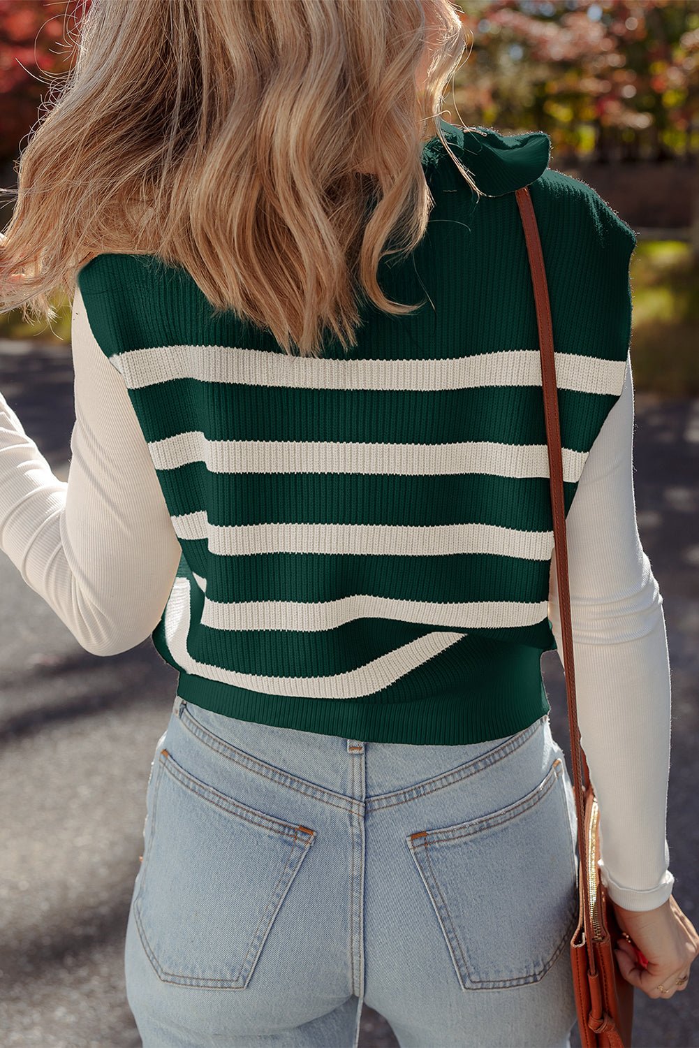 Person wearing a green and white striped sweater vest with light blue jeans outdoors.