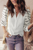 Woman wearing a white blouse with rolled-up sleeves, striped cardigan, and jeans, holding a beige handbag.