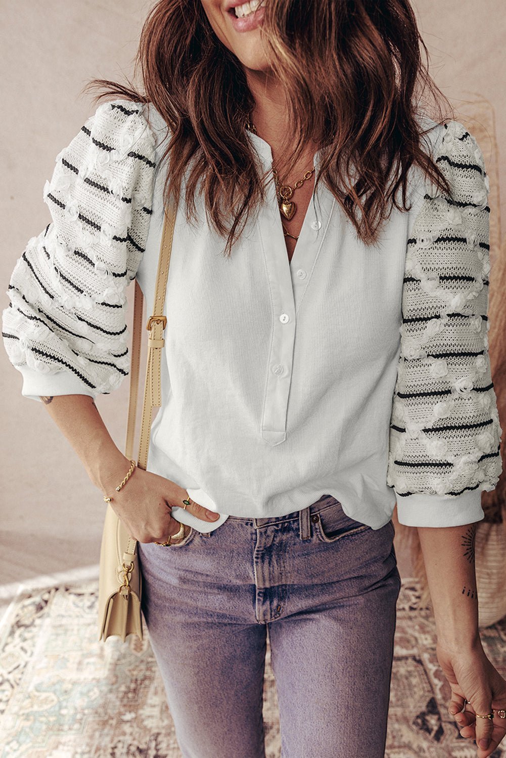 Woman wearing a white blouse with black patterns, purple jeans, and a beige bag.