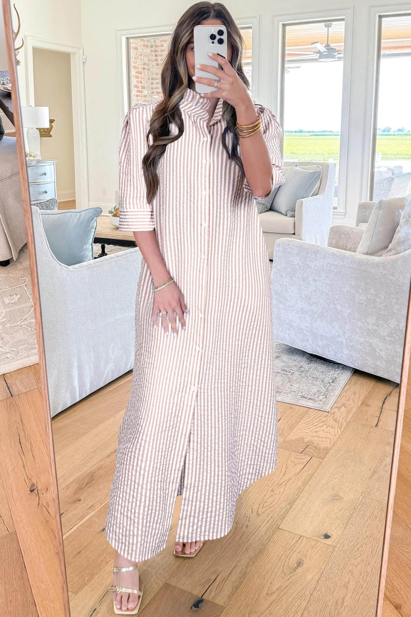 Woman taking a mirror selfie wearing a striped dress in a living room.