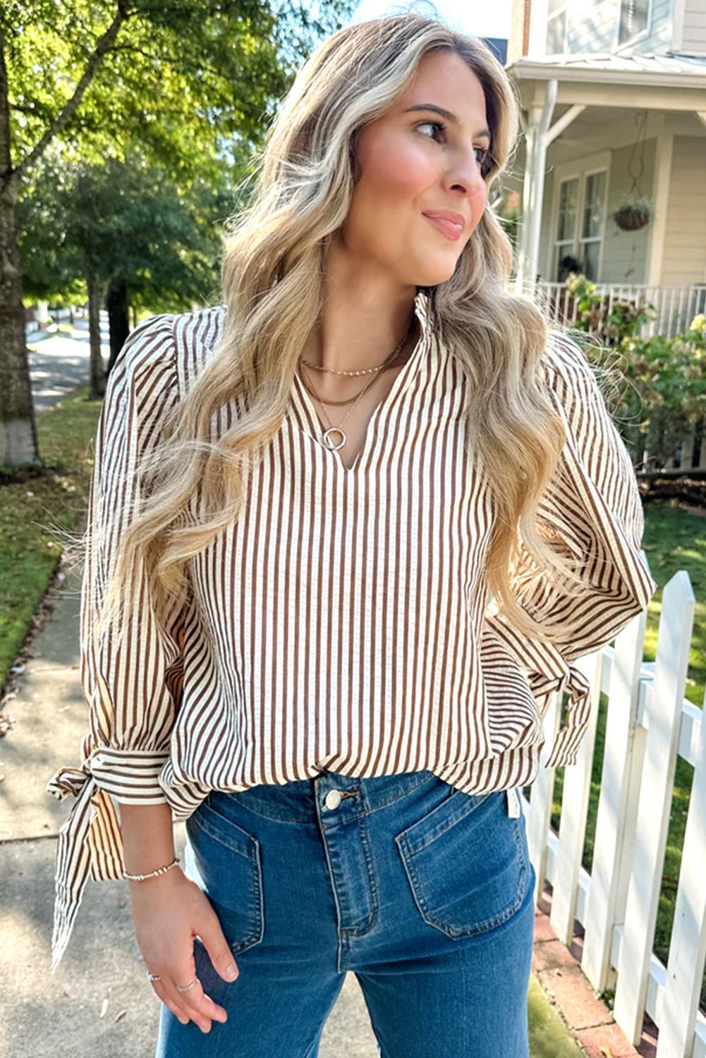 Woman wearing a striped shirt and blue jeans standing outdoors.