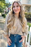 Woman with long blonde hair wearing a striped shirt and blue jeans standing outdoors.