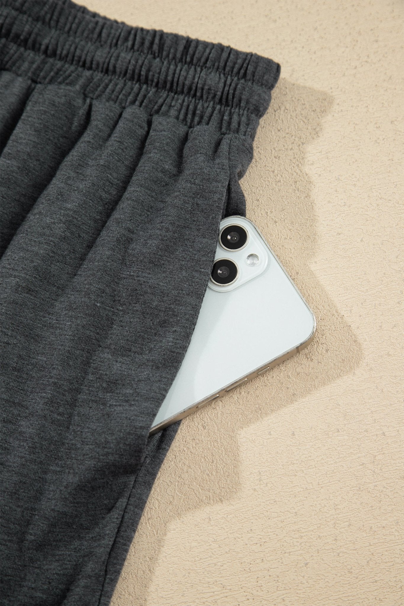 Close-up of dark gray heathered sweatpants with elastic waist and smartphone in side pocket.