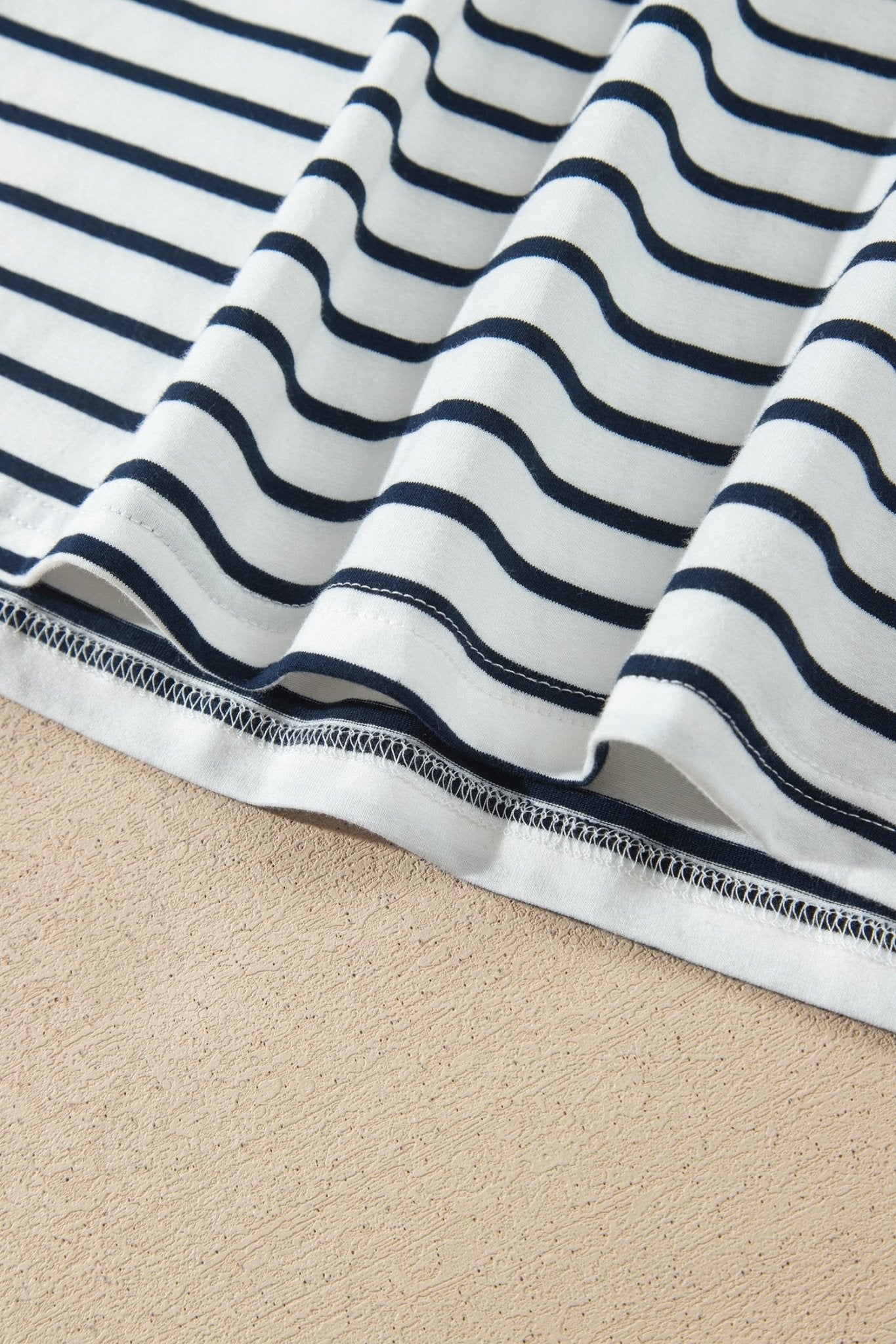Close-up of white fabric with navy wavy stripes, folded to show the stitched hem.