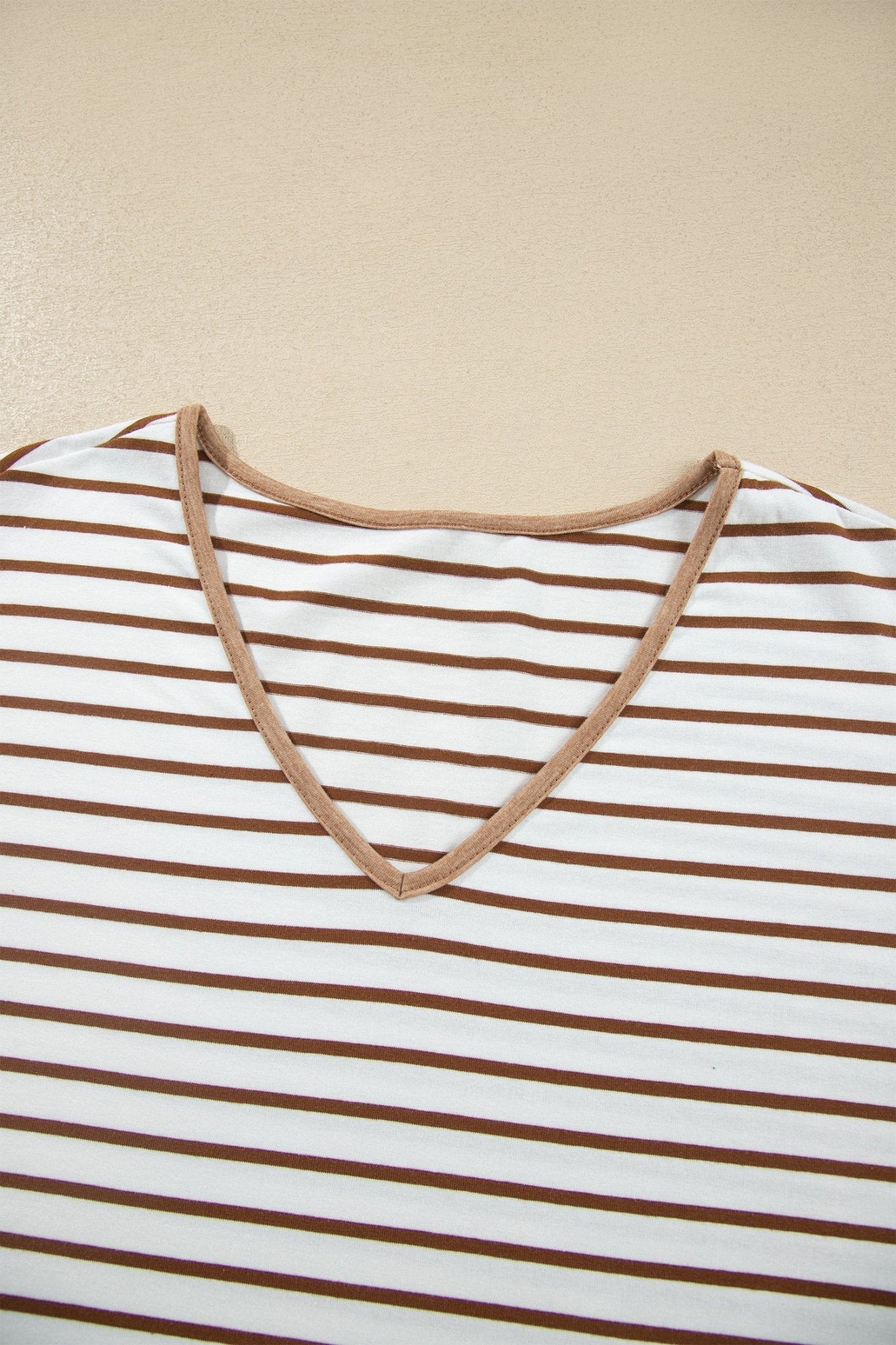 Close-up of a white V-neck top with brown stripes and contrasting brown neckline trim.