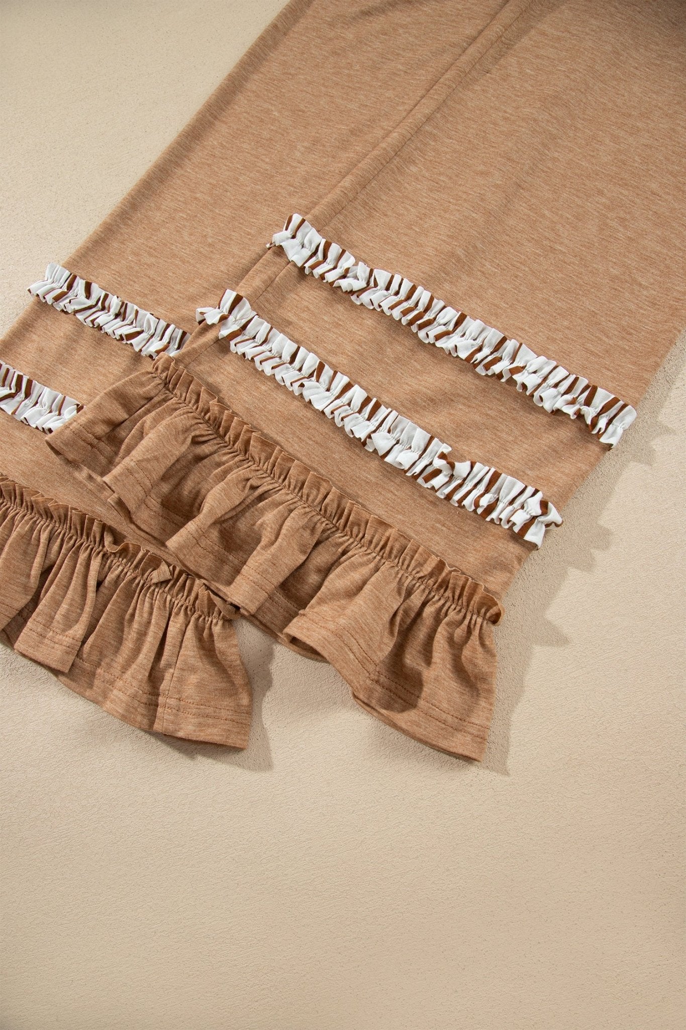 Close-up of a tan knit garment with white ruffled trim, black zigzag patterns, and gathered hem.