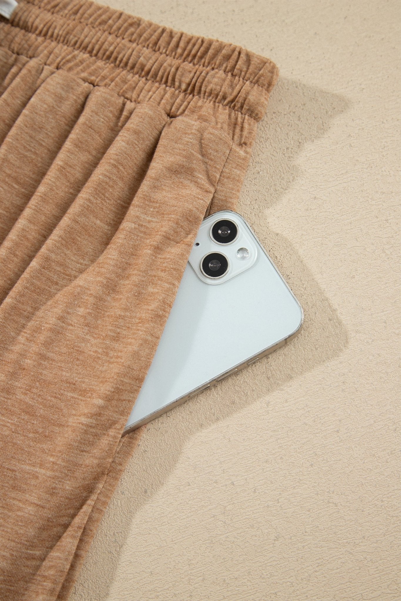 Close-up of tan drawstring shorts with a white smartphone peeking from the side pocket.