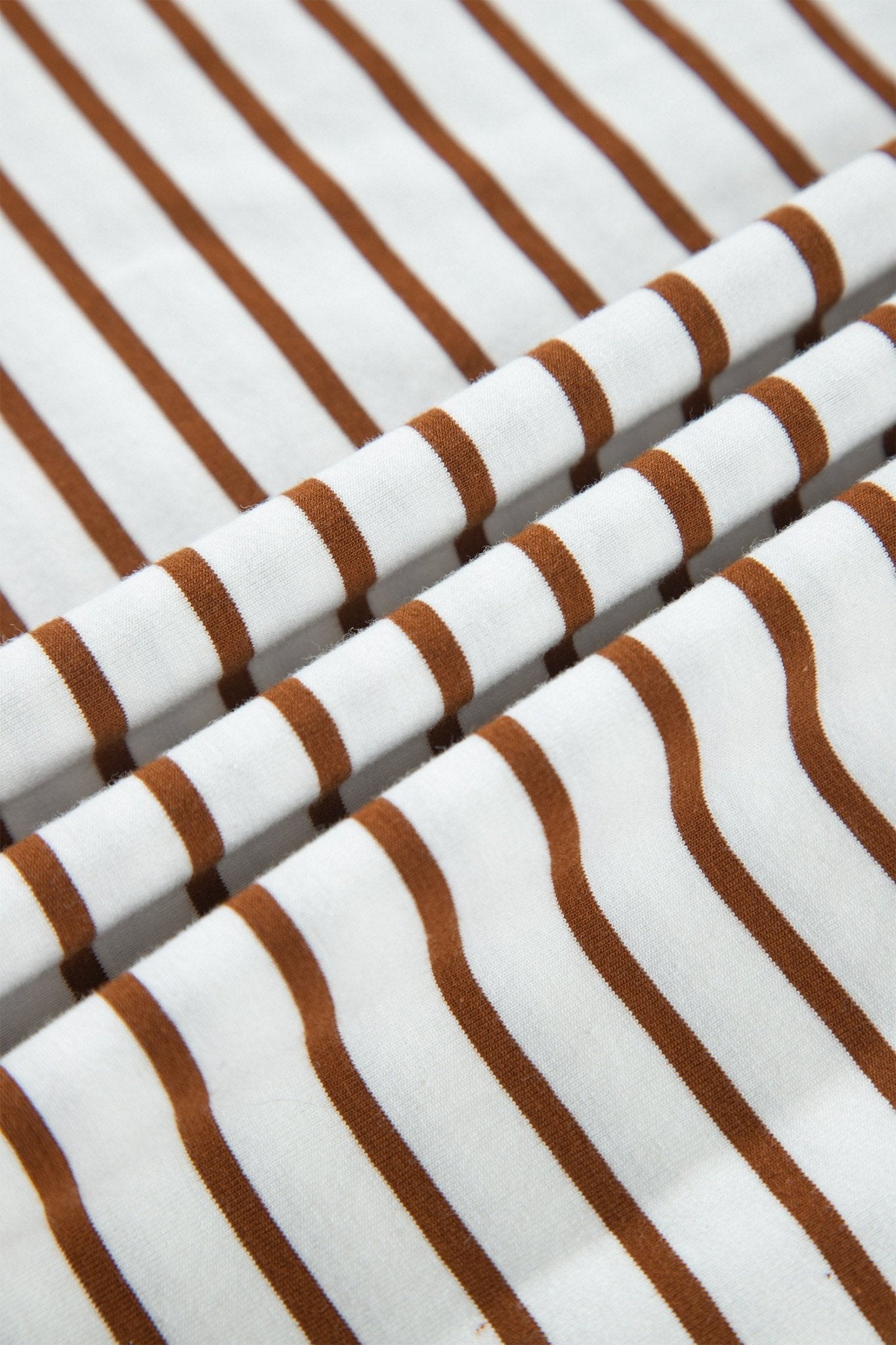 A close-up of white fabric with evenly spaced, slightly wavy brown stripes, shown in soft folds.