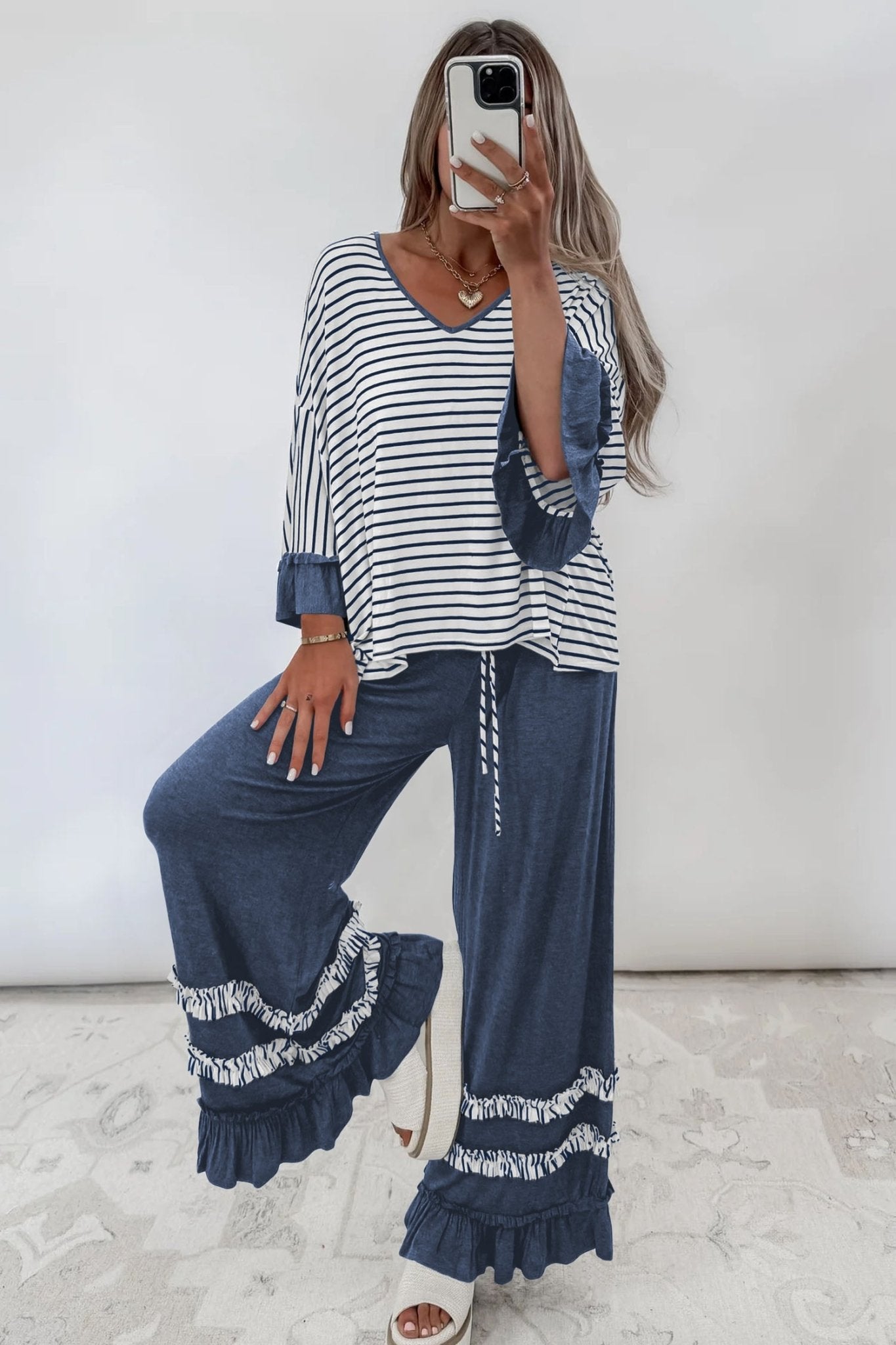 Woman taking a mirror selfie in a navy striped top with ruffled cuffs and wide-leg pants.