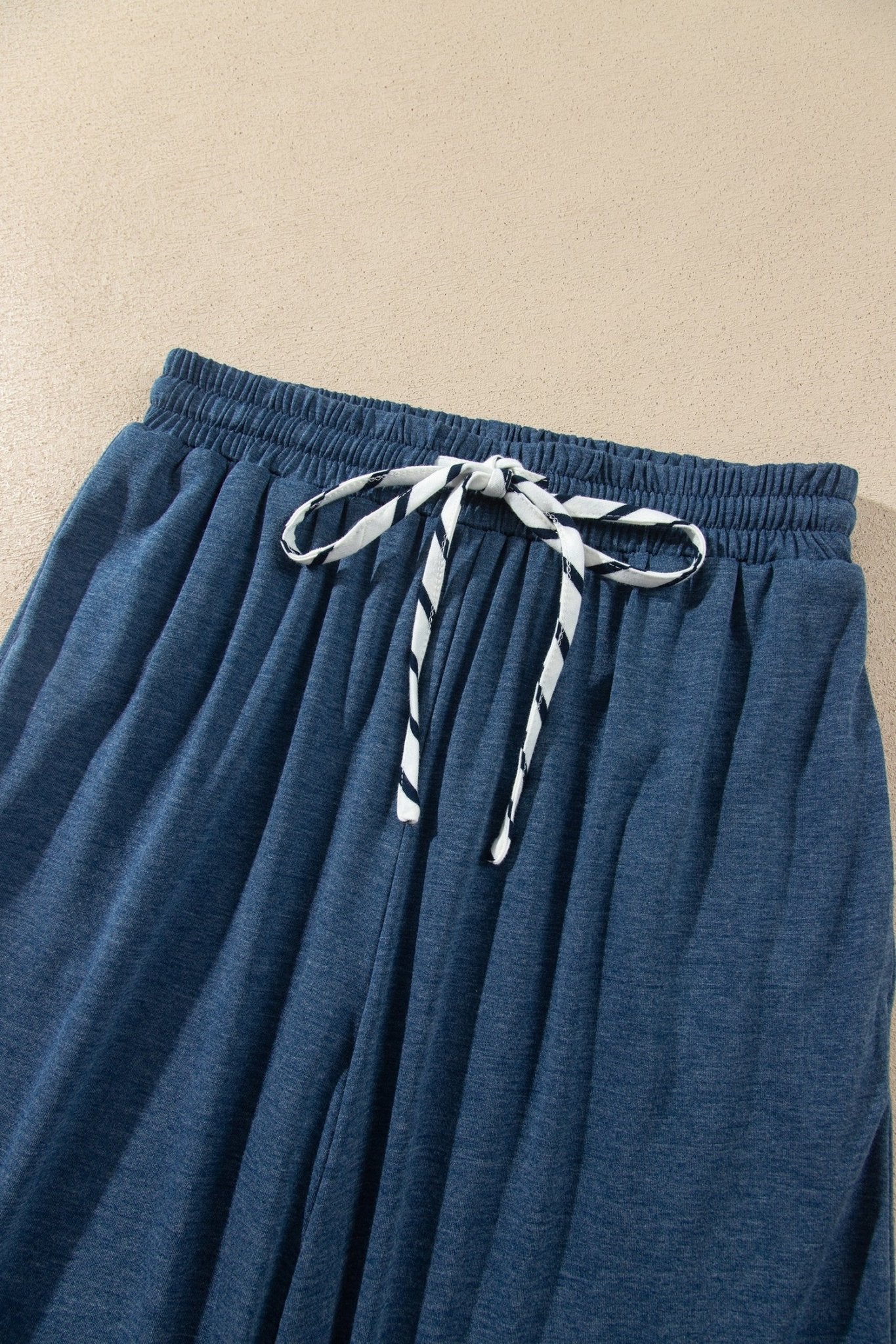 Close-up of blue pleated lounge pants with elastic waist and white-blue striped drawstring.