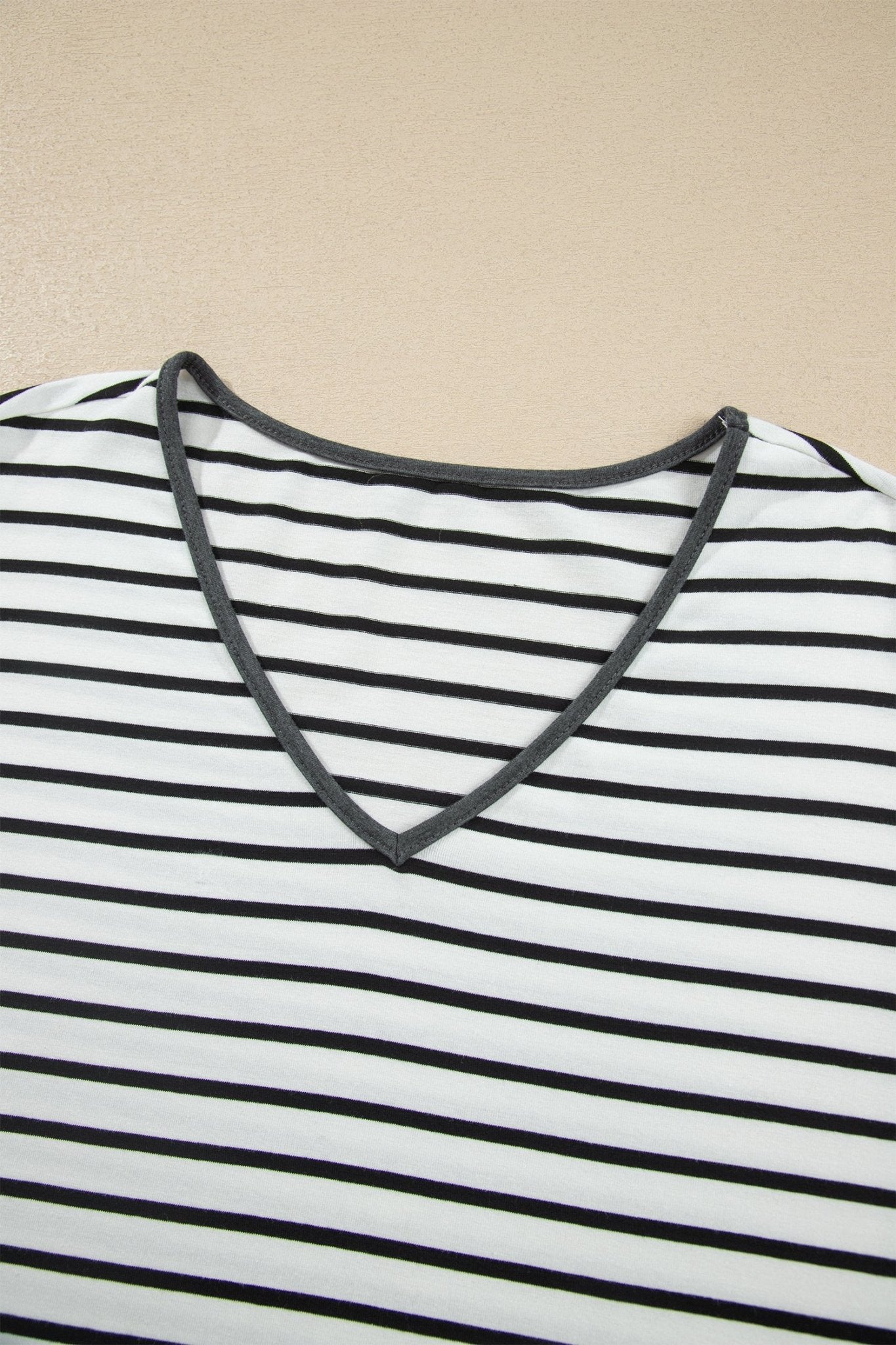 Close-up of a black and white striped V-neck top with dark gray trim on a beige background.