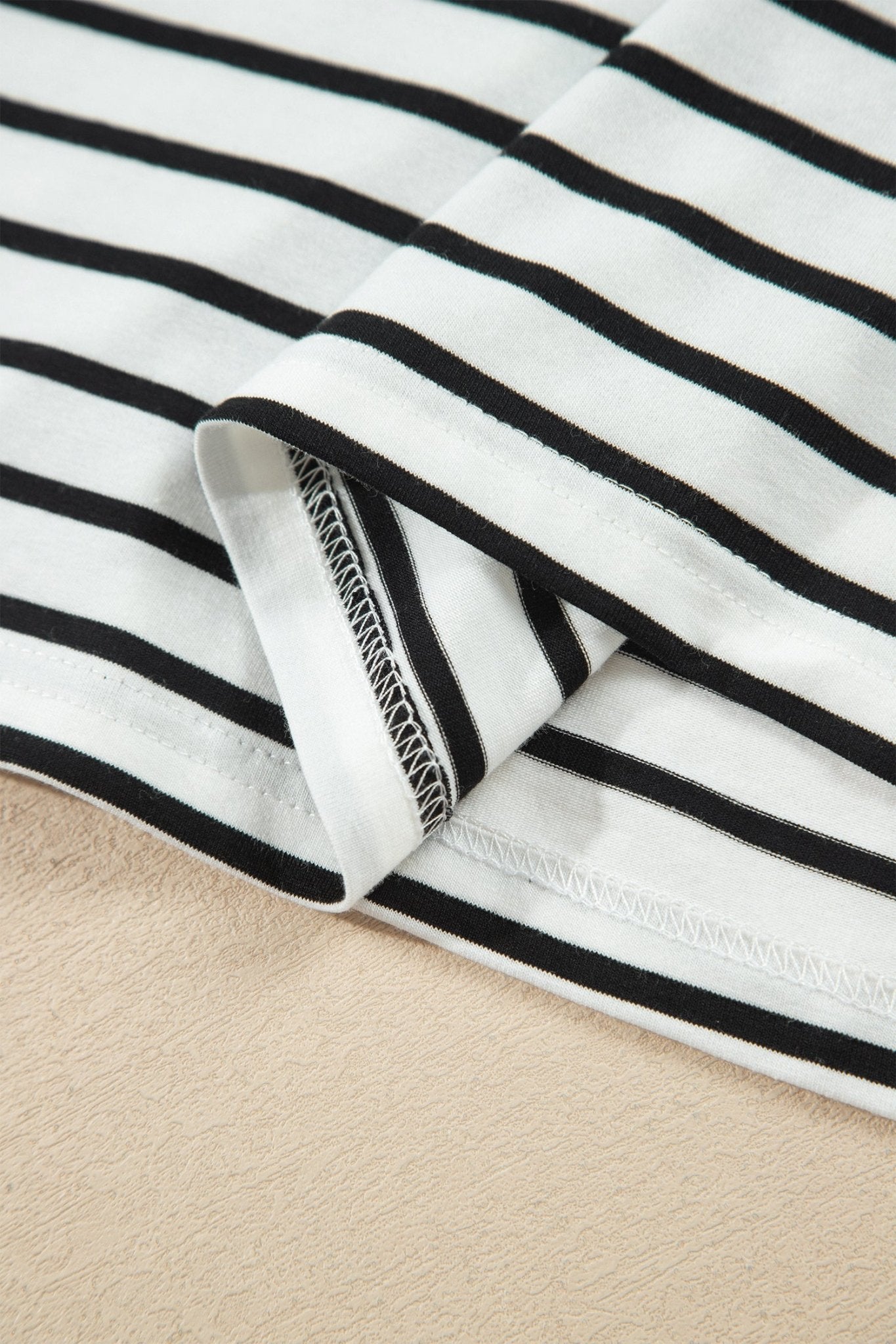 Close-up of white fabric with thin black stripes, folded to show texture and hem stitching.