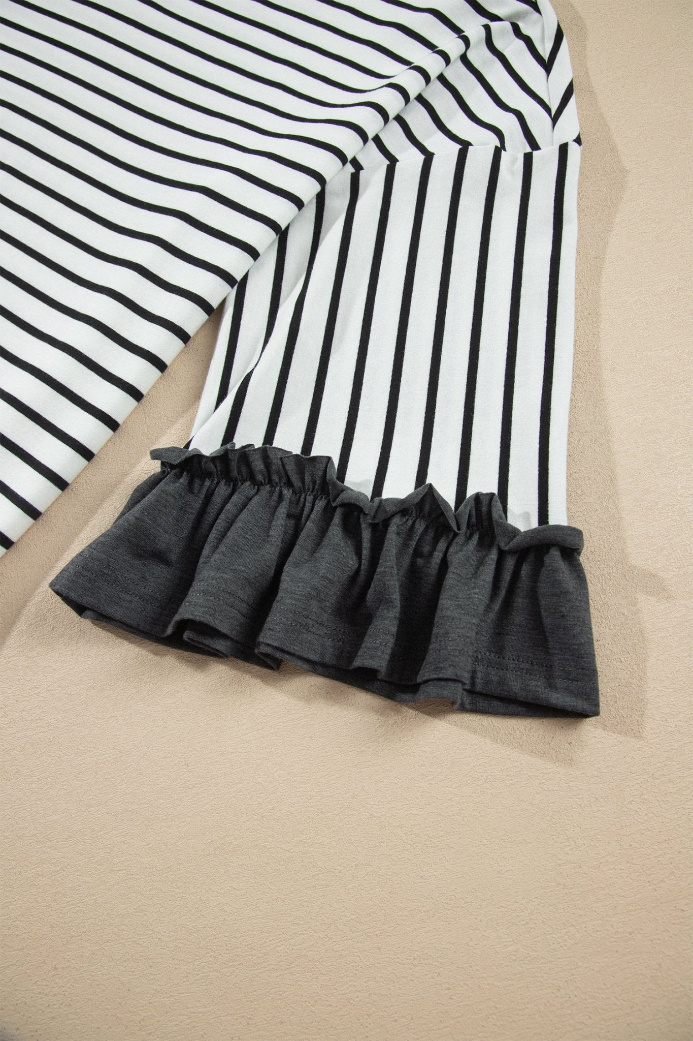 Close-up of black and white striped fabric with a gathered dark gray ruffle hem.