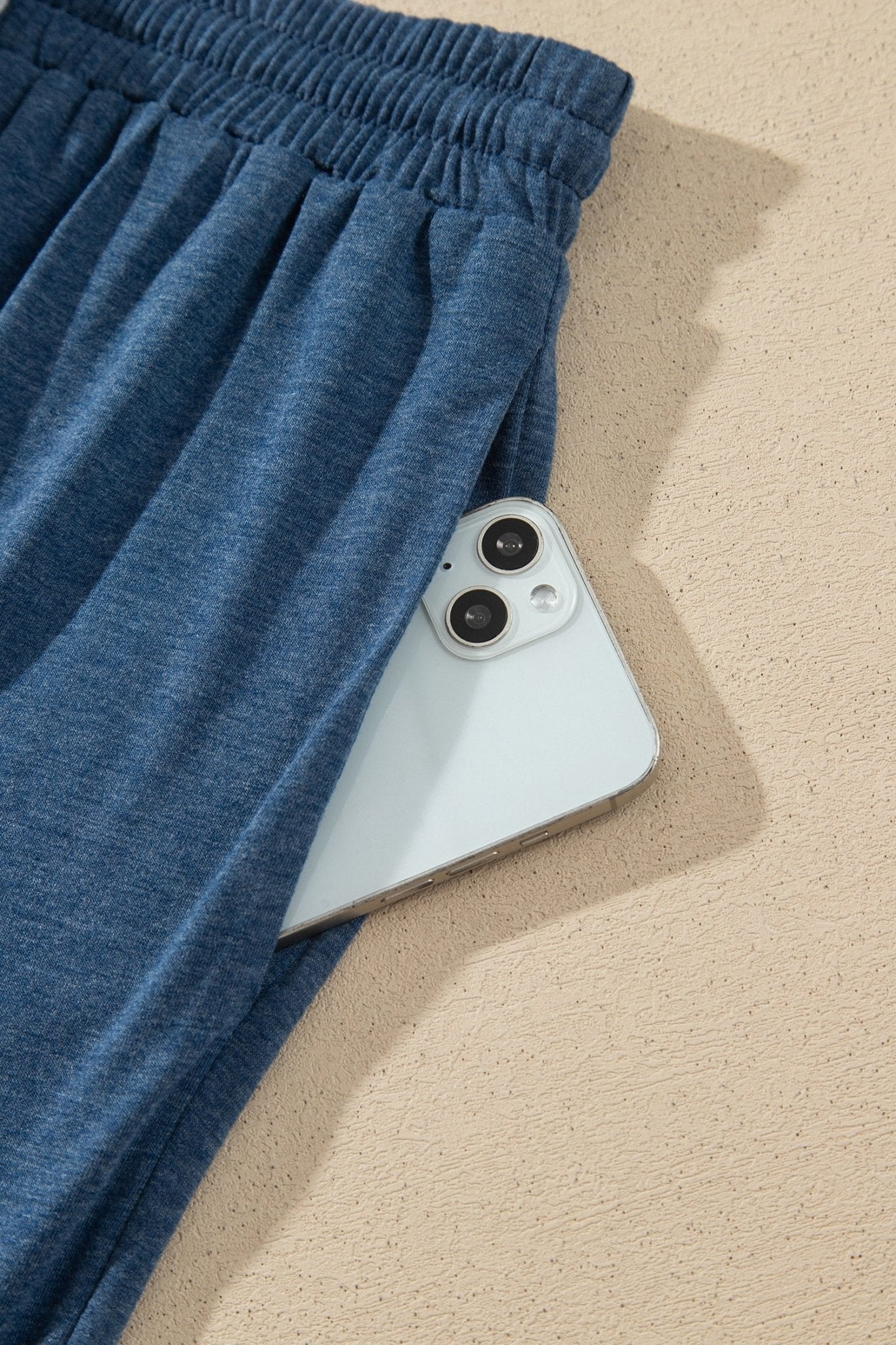 Close-up of blue heathered lounge pants with elastic waistband and smartphone in side pocket.