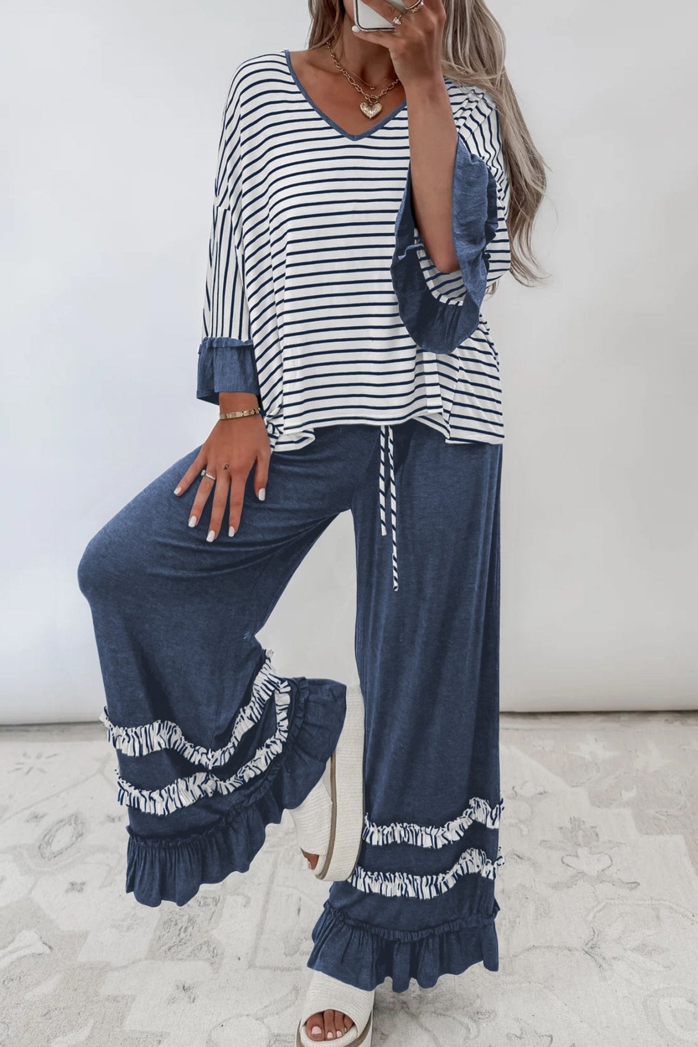 Woman modeling a navy striped top with ruffled cuffs and wide-leg pants with fringe hems.