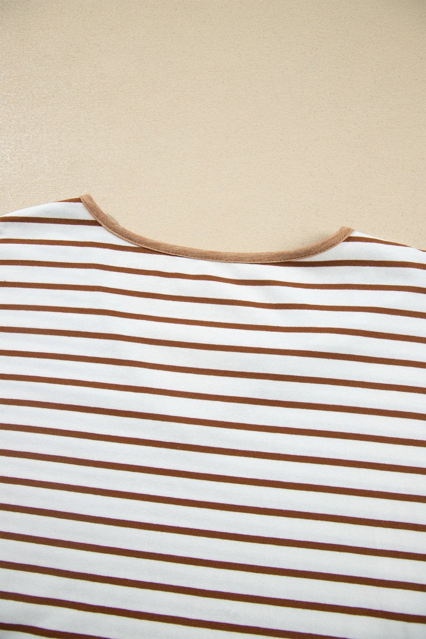 Close-up of a white striped garment with thin brown stripes and a brown neckline trim.