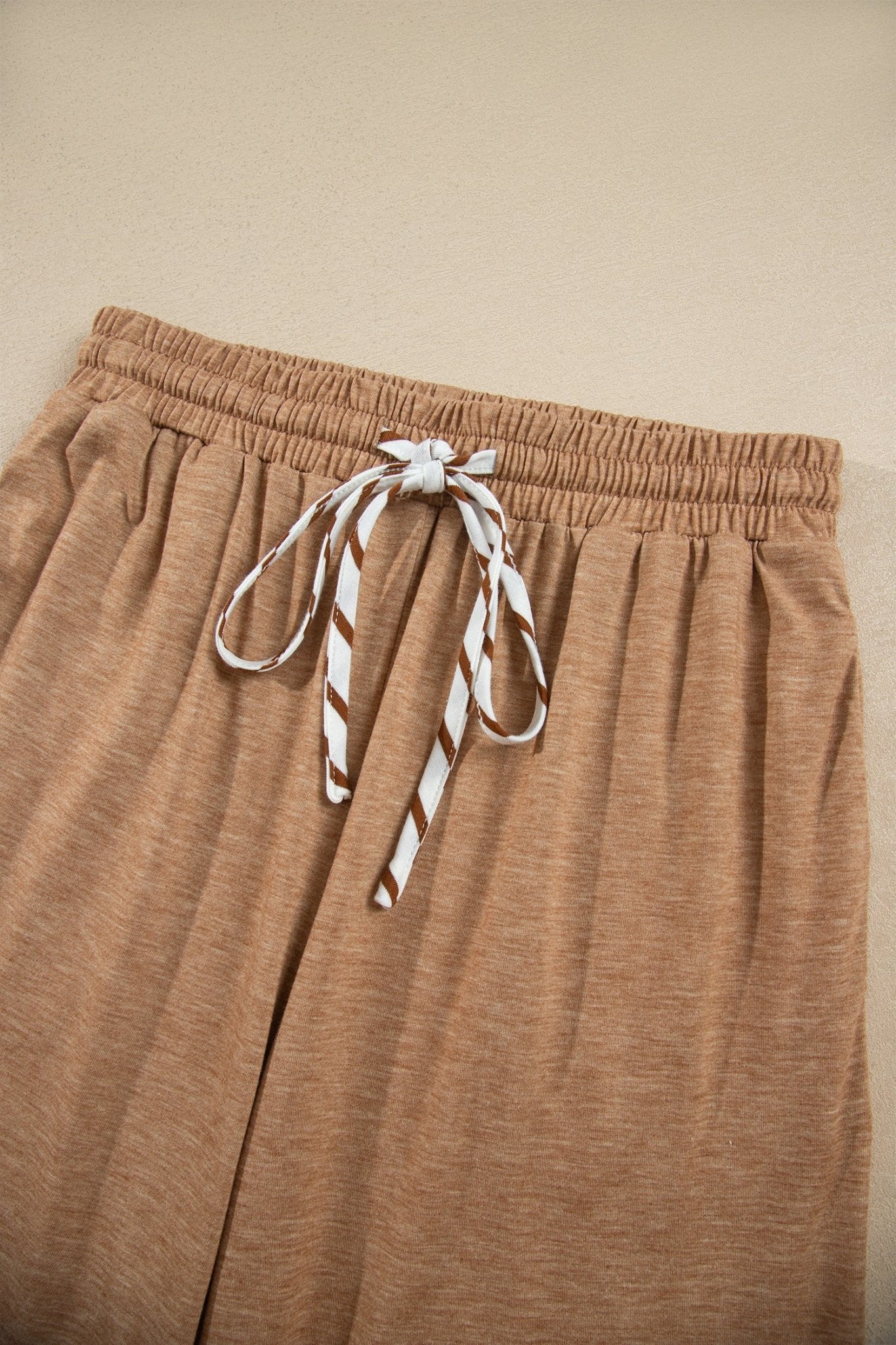 Close-up of heathered tan lounge pants with an elastic waist and striped drawstring.