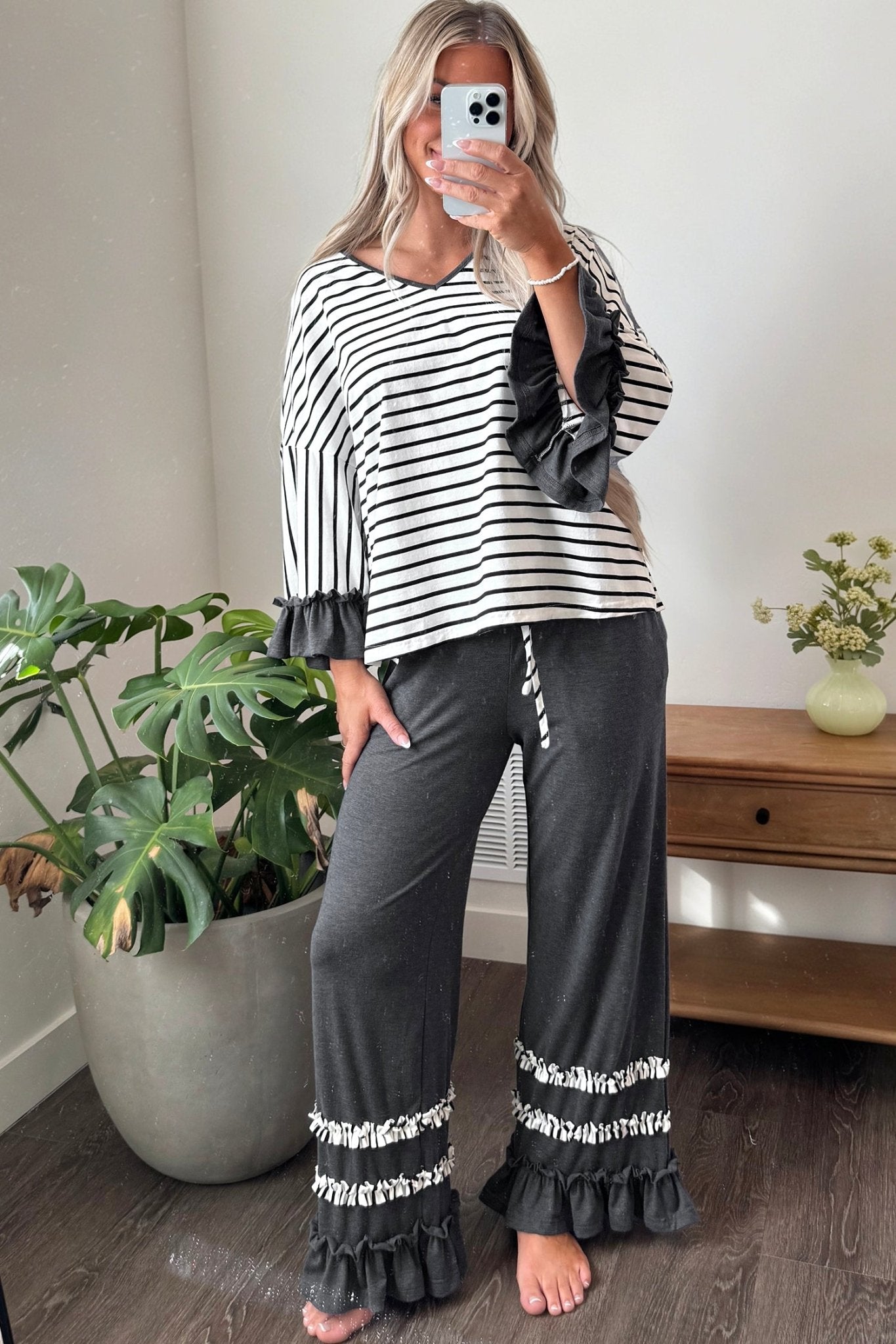 Woman wearing a black and white striped top with dark gray wide-leg ruffle-trim pants.
