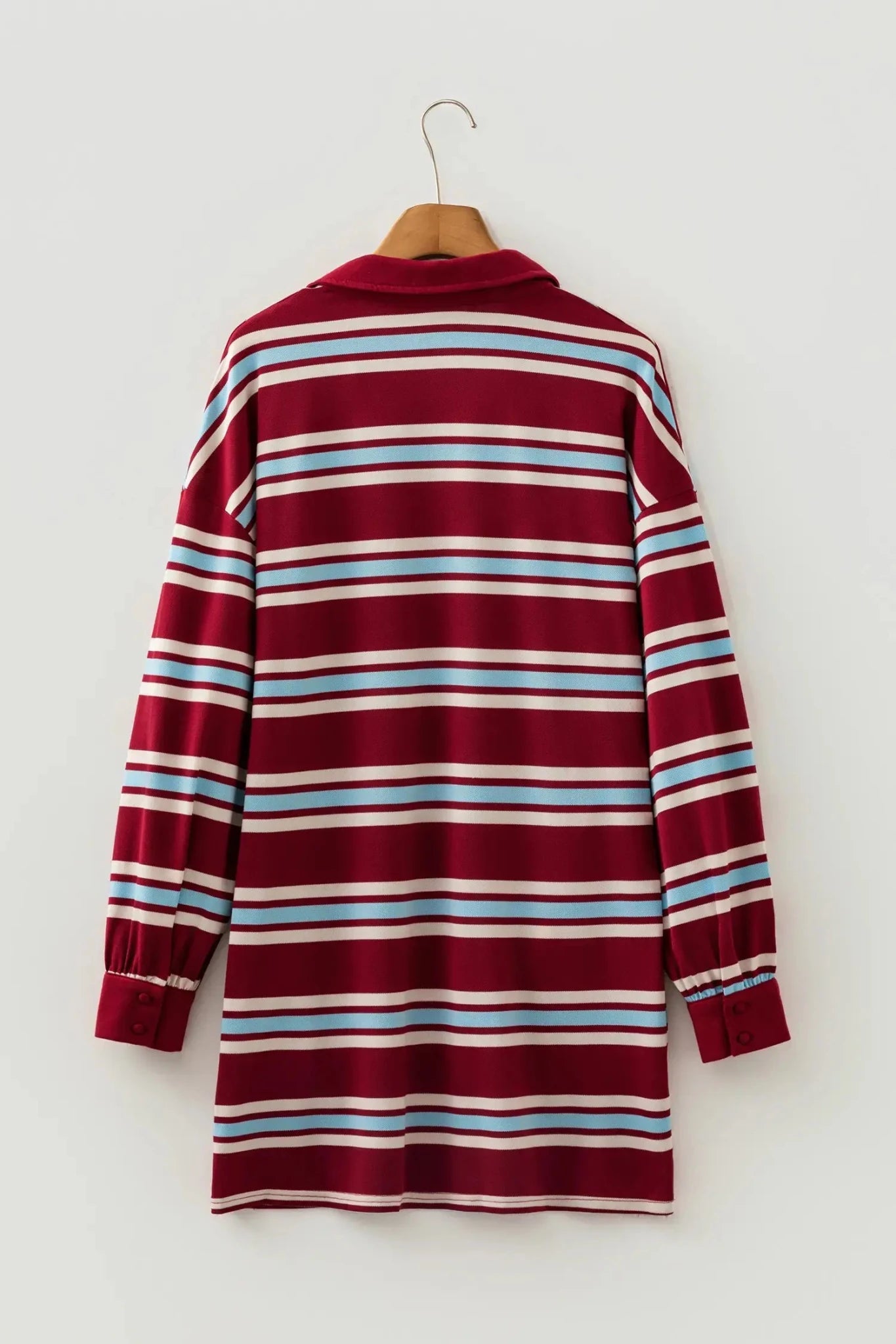 A long-sleeve collared shirt dress with horizontal stripes in burgundy, white, light blue, and thin red stripes, hanging on a wooden hanger against a light gray wall.