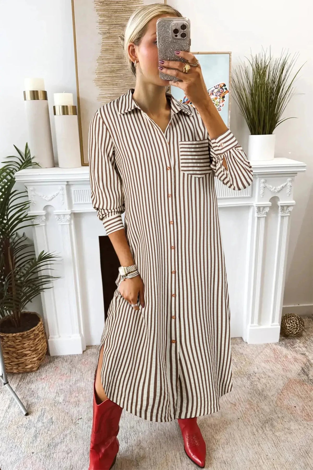 Woman taking a mirror selfie wearing a striped dress and red boots in a home setting.