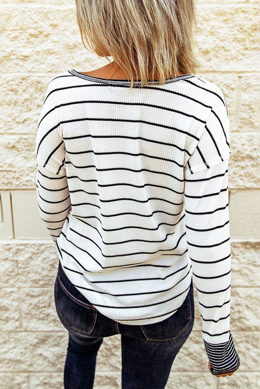 Person wearing a black and white striped sweater against a stone wall.