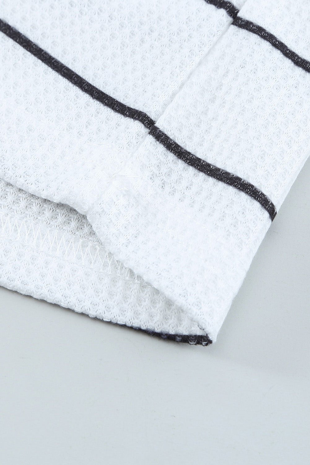 Close-up of a white fabric with black trim on a light gray background