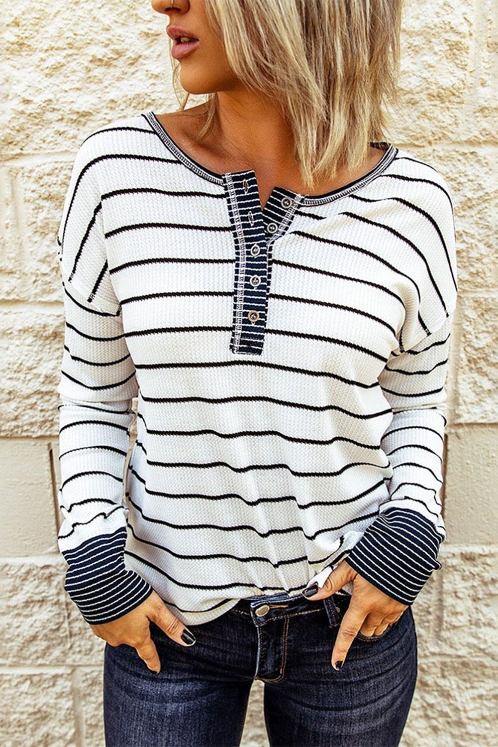 Person wearing a black and white striped long-sleeve shirt against a stone wall.