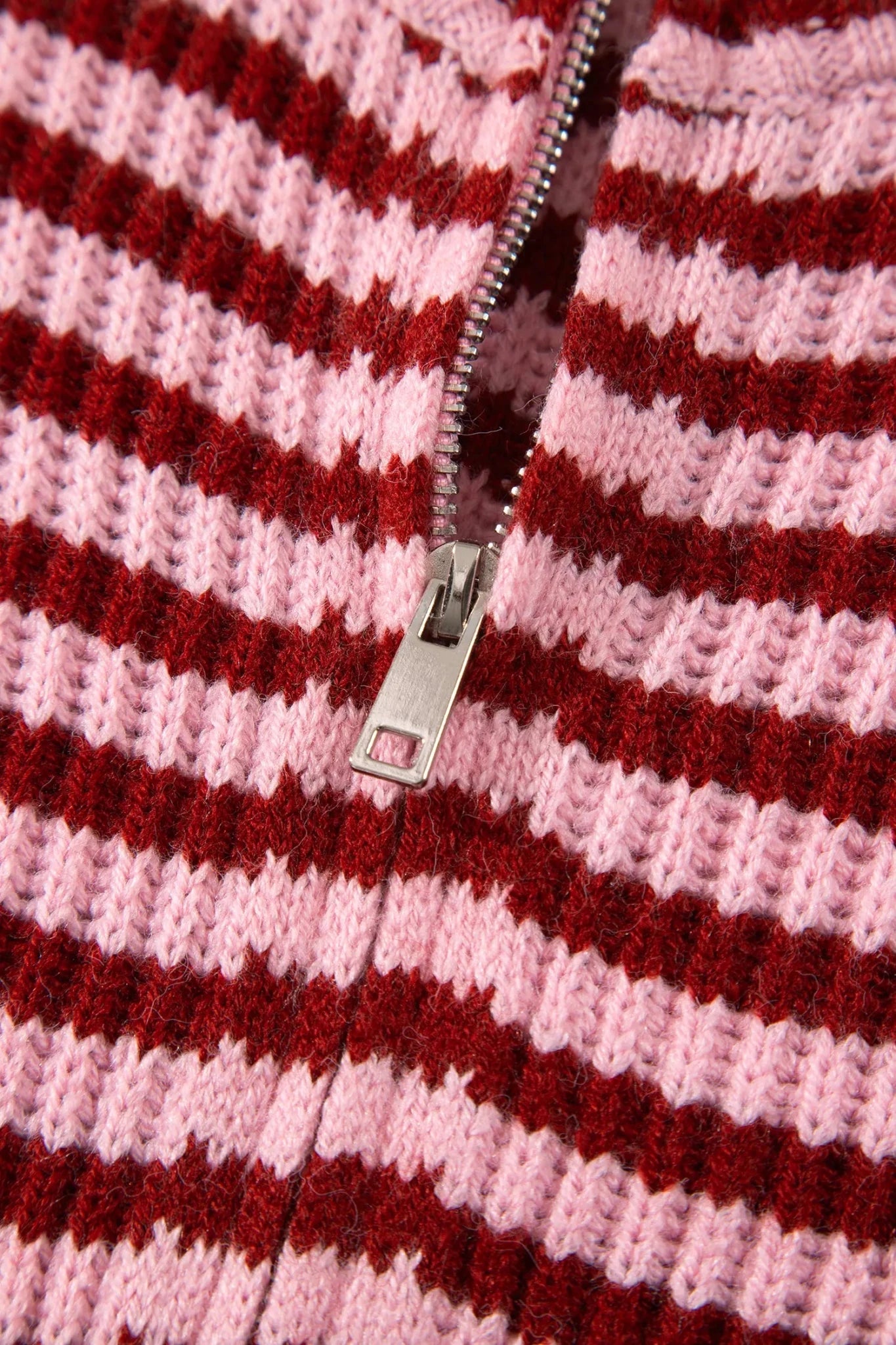 Close-up of dark red and light pink striped knit sweater with silver zipper pull.