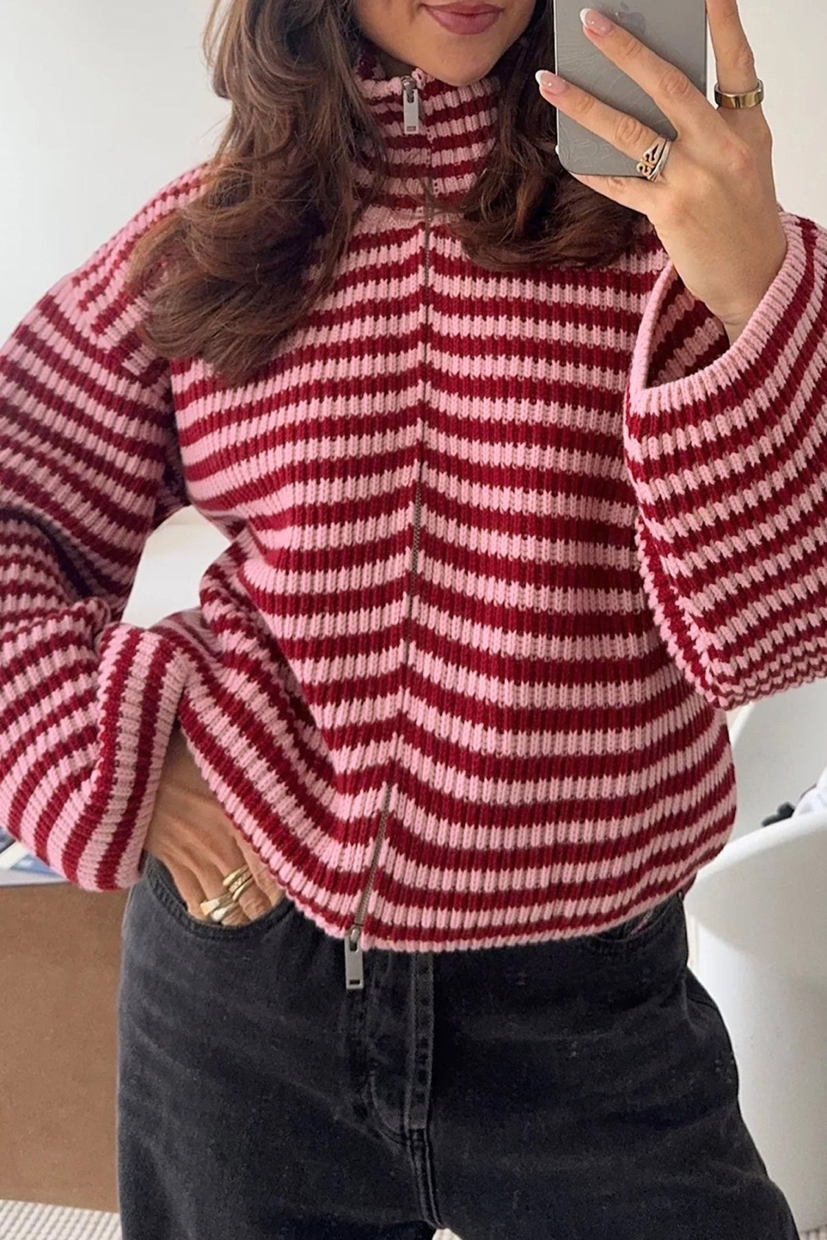 Woman in red-white striped quarter-zip knit sweater and black jeans, mirror selfie.