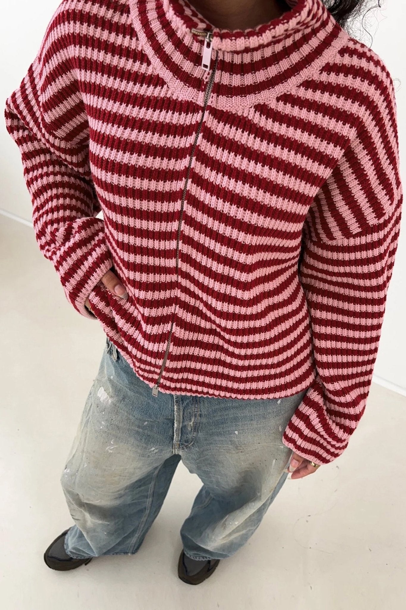 Person in red-pink striped zip-up knit sweater, light-wash jeans, and black shoes.