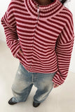 Person in red-pink striped zip-up knit sweater, light-wash jeans, and black shoes.