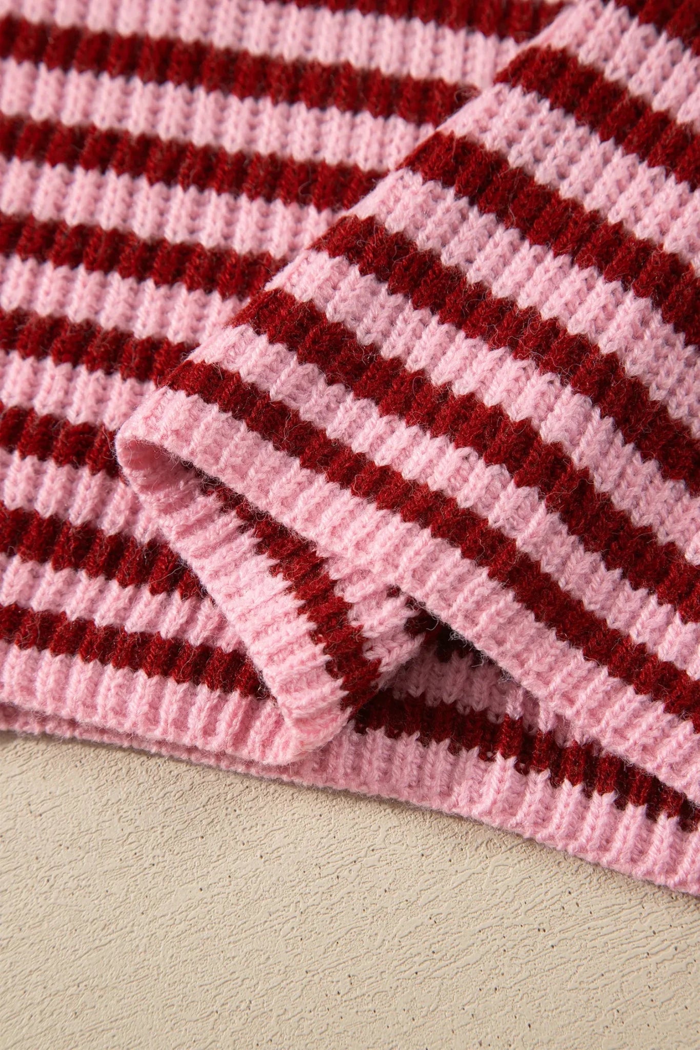 A close-up of a pink and dark red striped knit fabric, folded to show the ribbed texture and pattern.