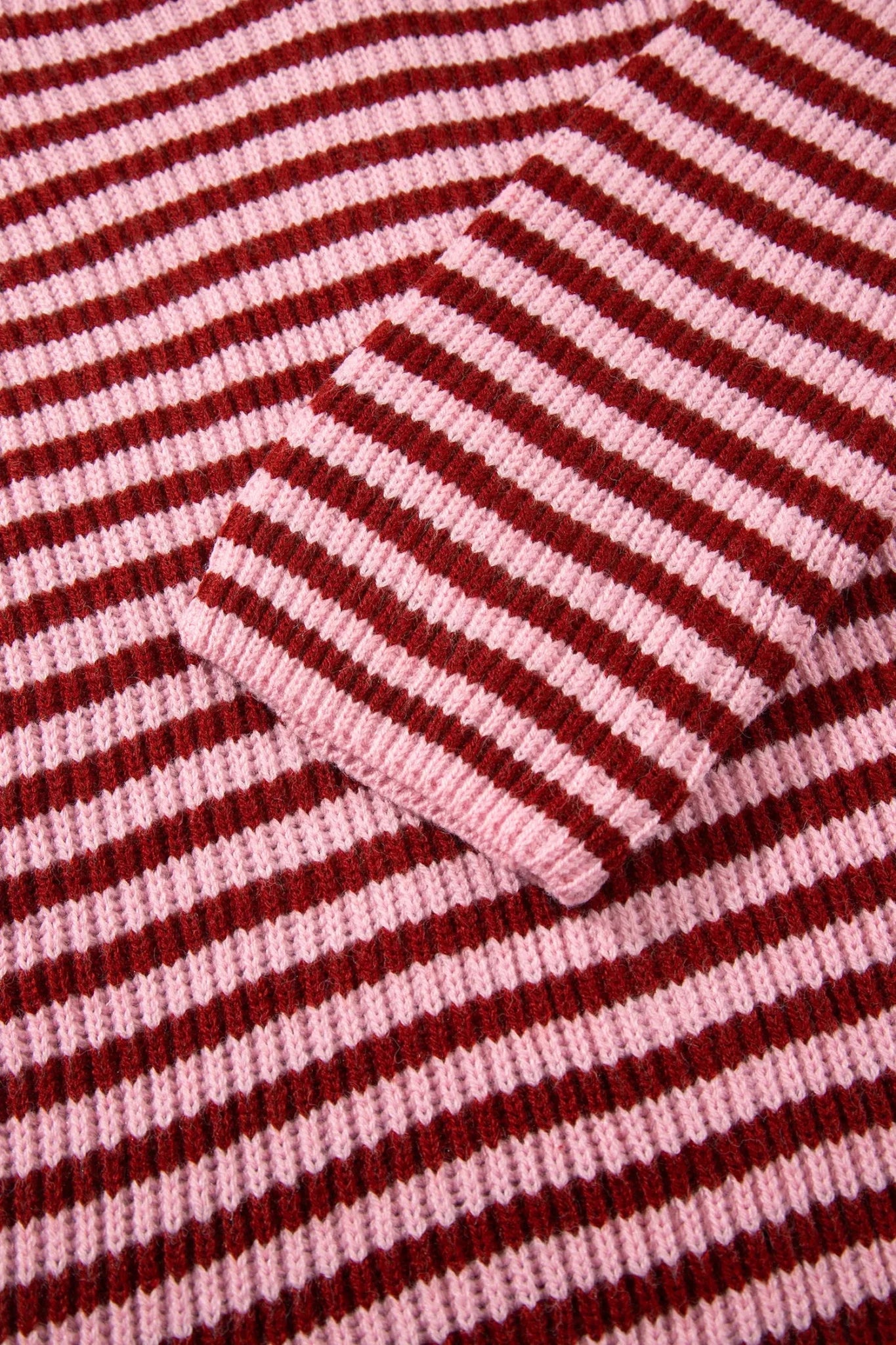 Close-up of dark red and light pink striped knit fabric with folded cuff detail.
