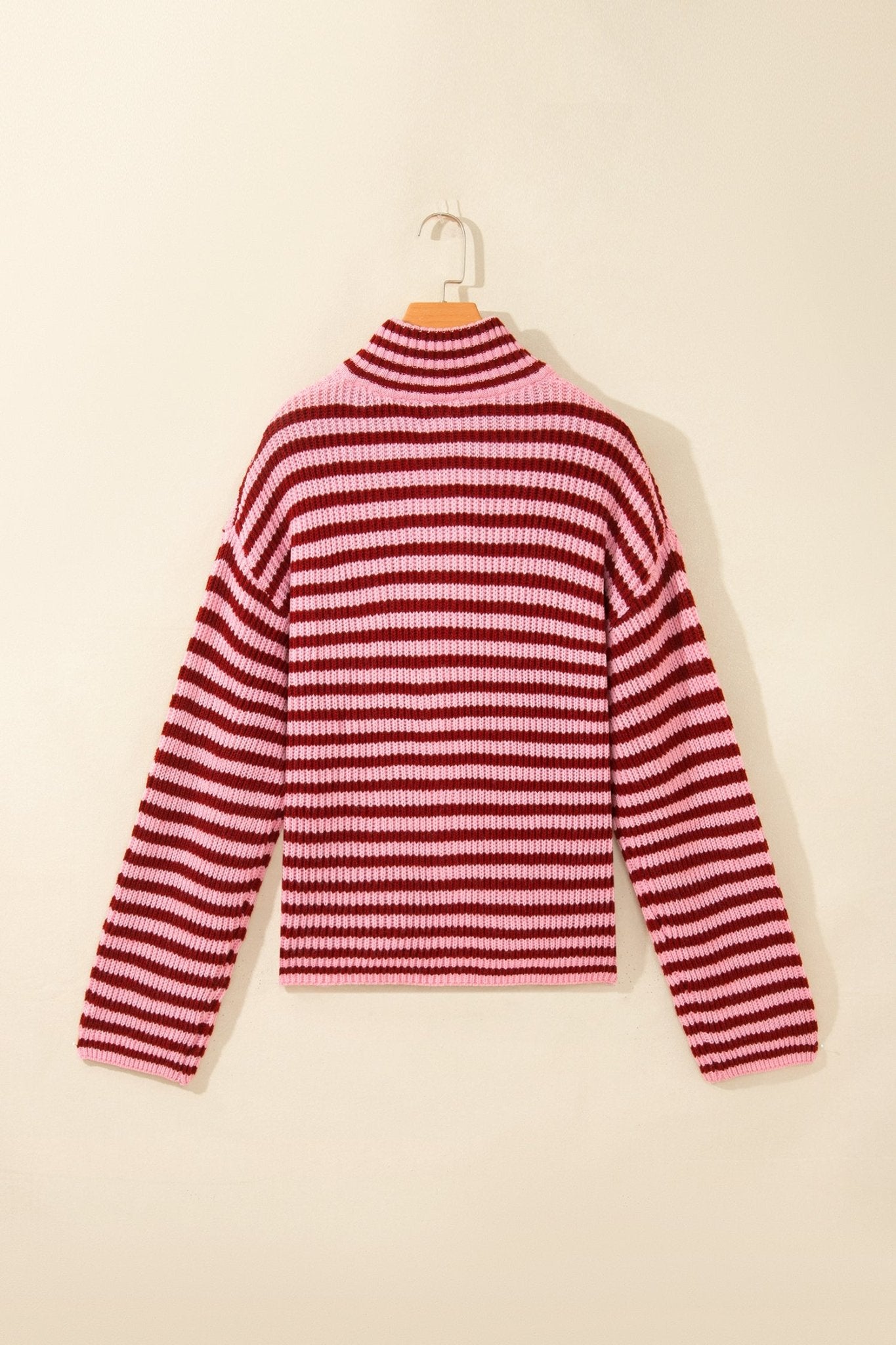 Pink-dark red striped knit mock-neck sweater hanging on a wooden hanger.