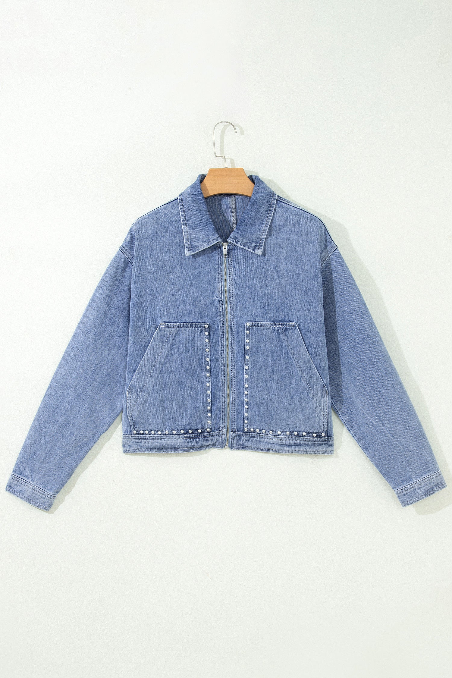 Light blue zip up cropped denim jacket with studded pockets on a hanger, front view