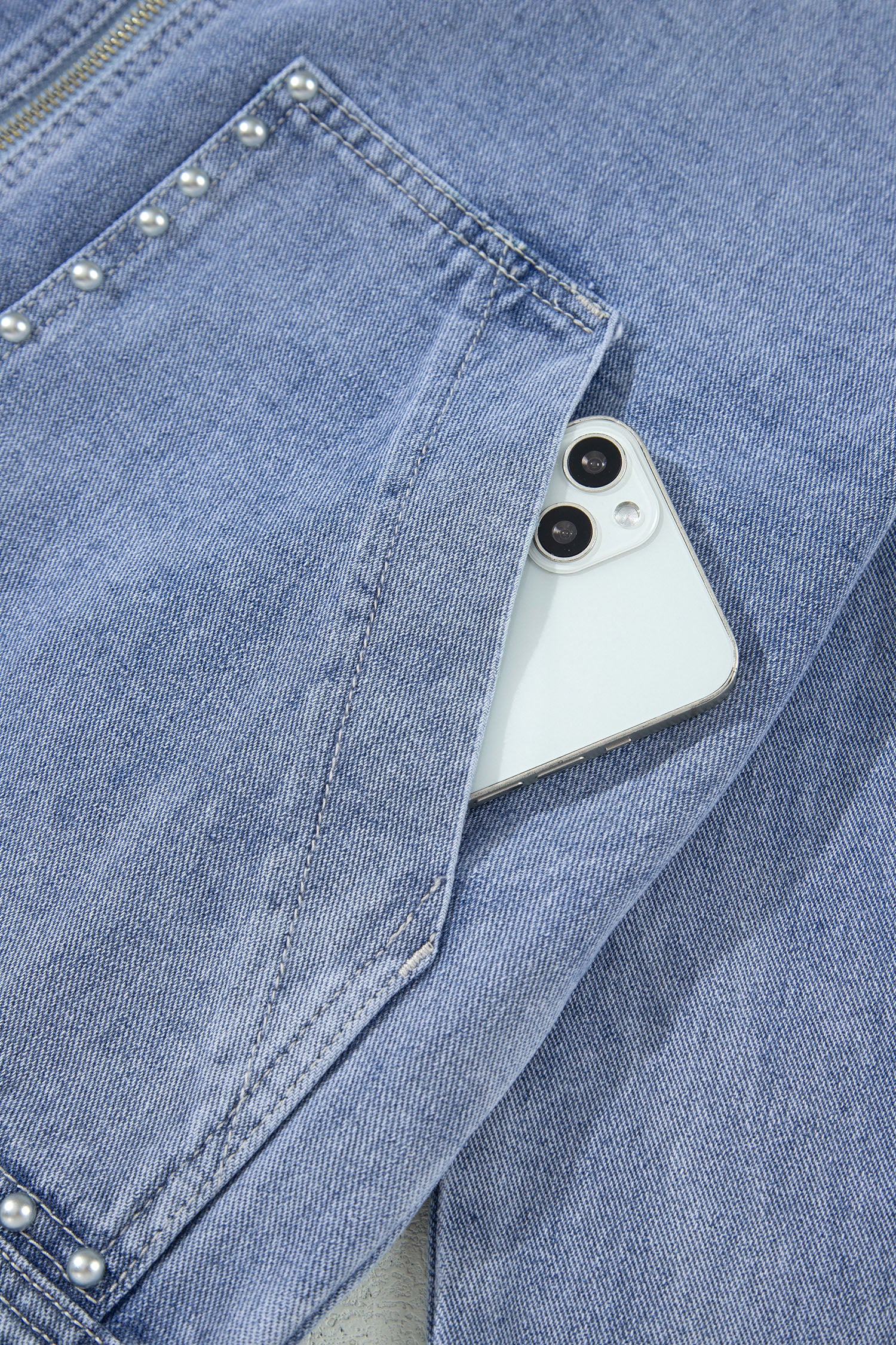 Light blue denim jacket studded patch pocket holding a phone