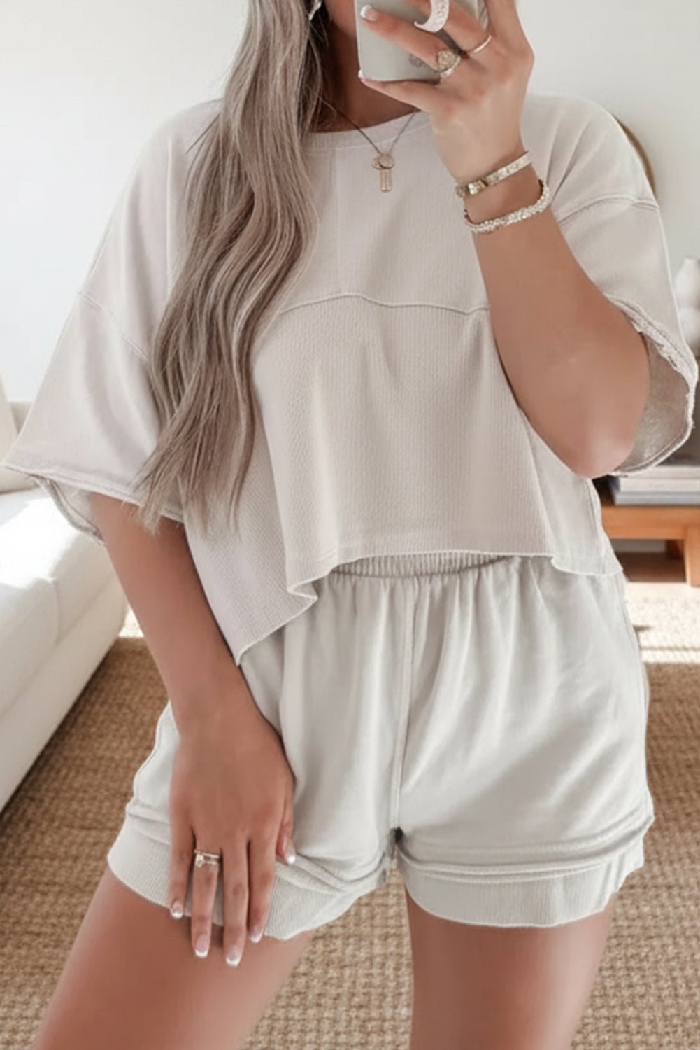 Person wearing a white outfit with shorts, holding a phone indoors.