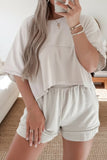 Person wearing a white outfit with shorts, holding a phone indoors.