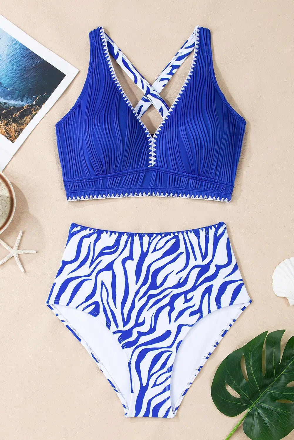 Blue and white patterned bikini set on a beige surface with a leaf and photo frame.