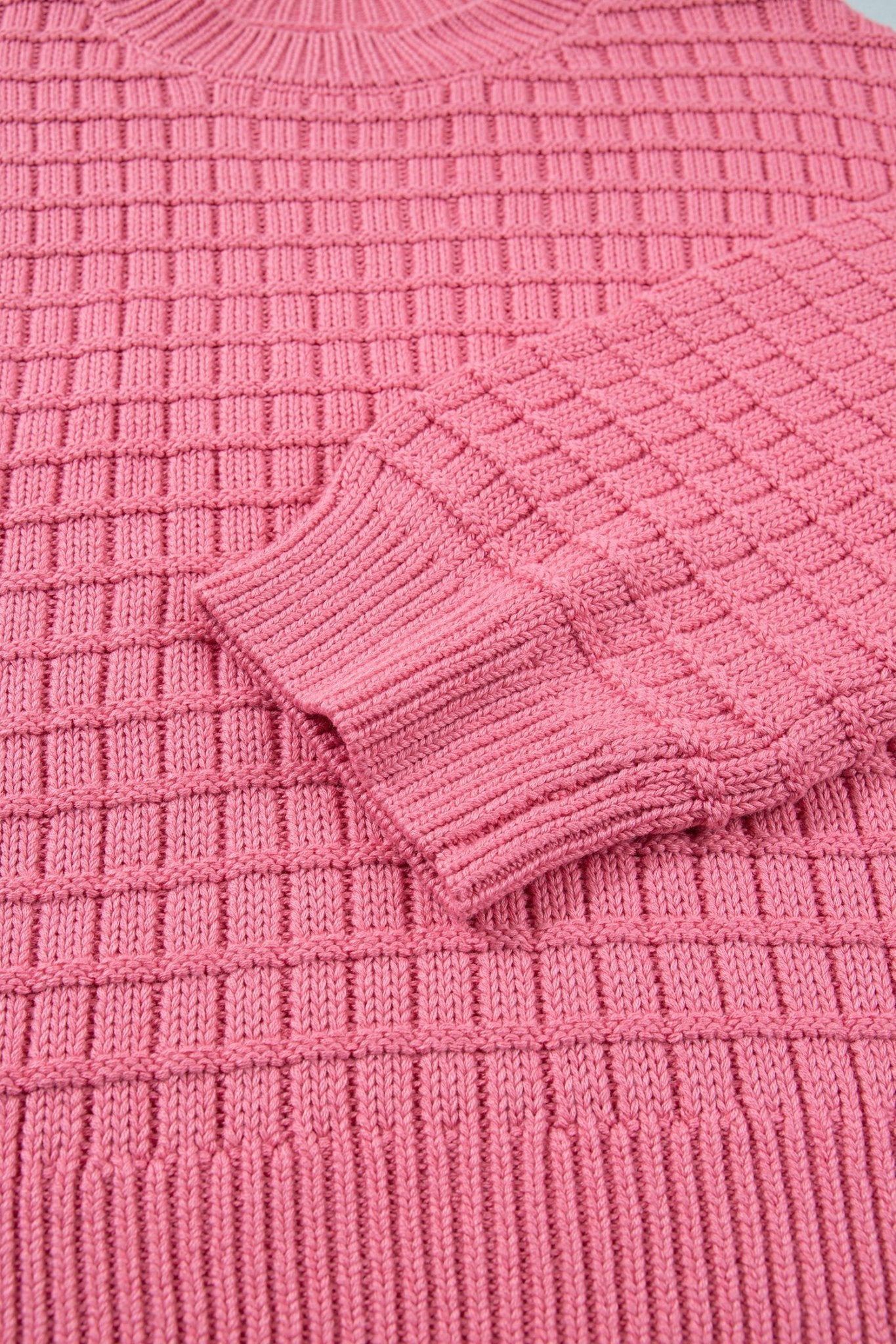 A close-up of a pink ribbed knit sweater showing the textured waffle pattern and folded cuff.