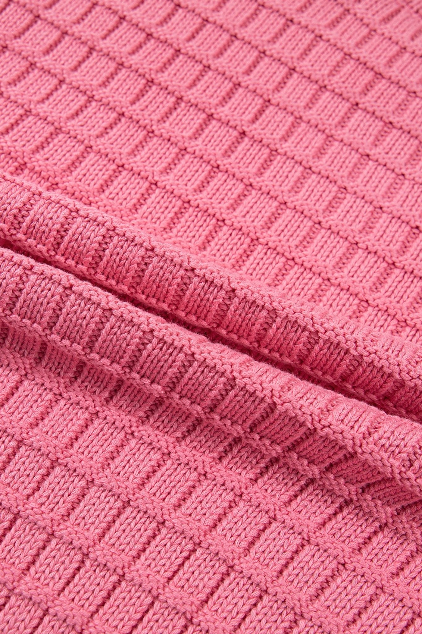 A close-up of a pink ribbed knit fabric, showing the detailed texture and a folded seam.