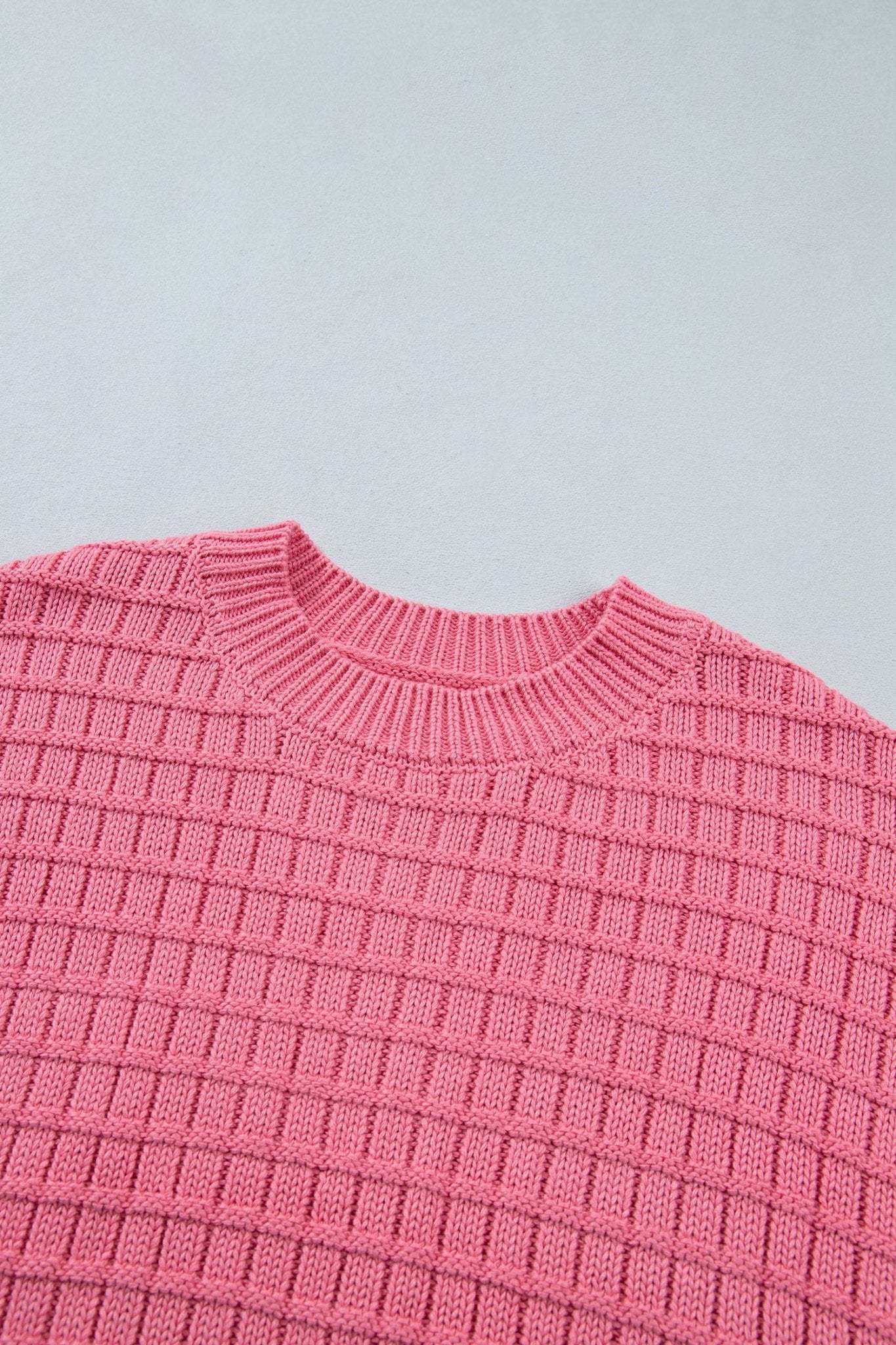 A close-up of a pink ribbed knit sweater showing the textured waffle pattern and crew neck collar.