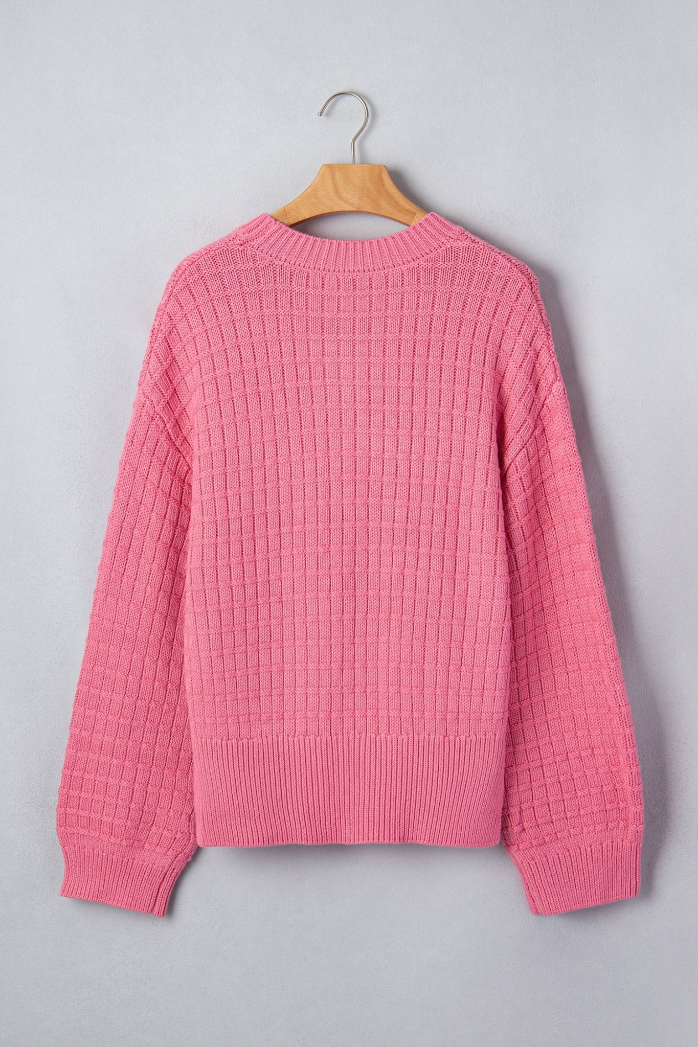 A pink textured knit sweater with a crew neck and ribbed cuffs and hem, hanging on a wooden hanger.