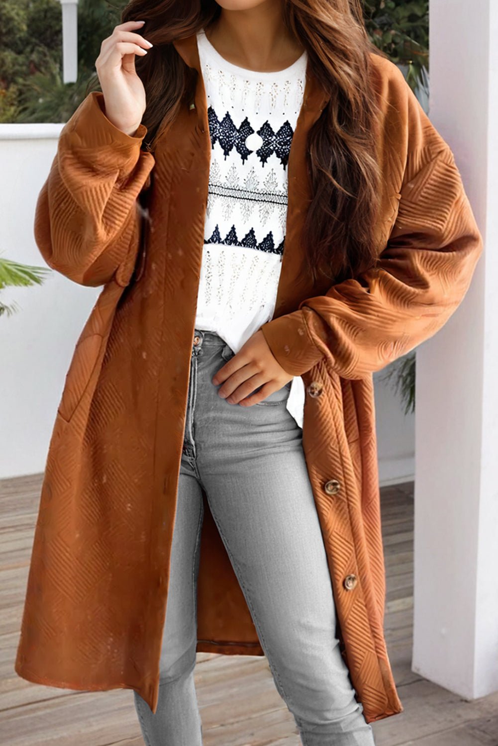 Person wearing a brown coat over a white sweater with black patterns and light blue jeans.