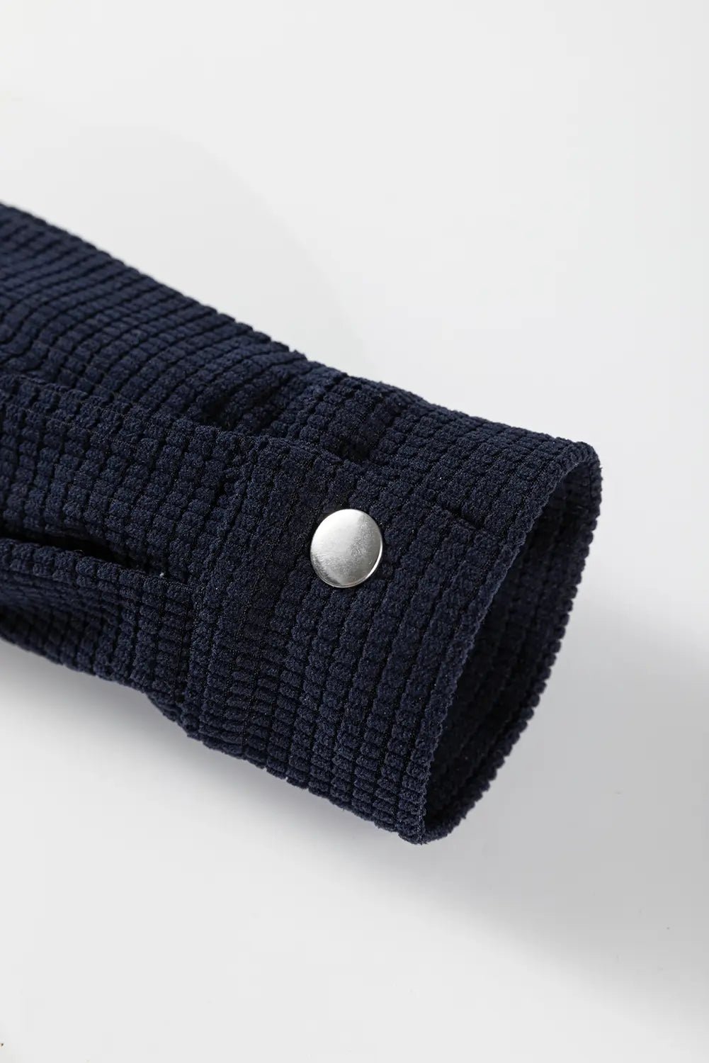 Close-up of a navy blue textured sleeve with a silver button on a light gray background