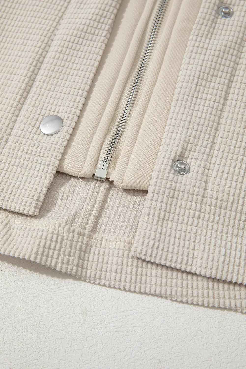 Close-up of textured beige fabric with a zipper and buttons against a light gray background.