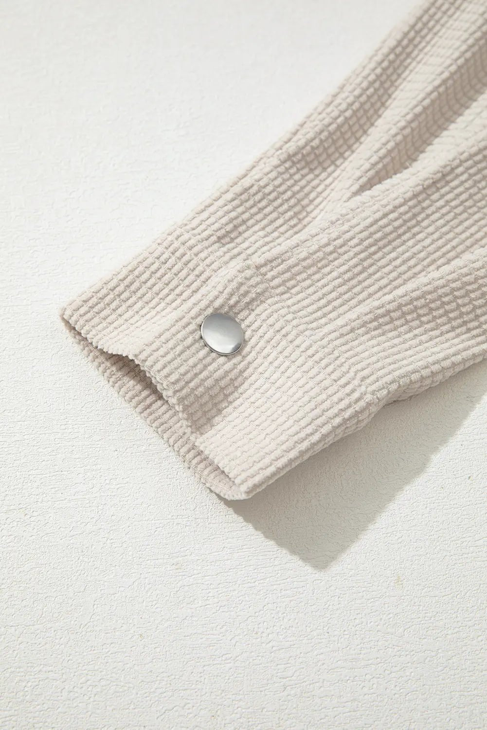 Close-up of a textured beige fabric with a button on a light background.