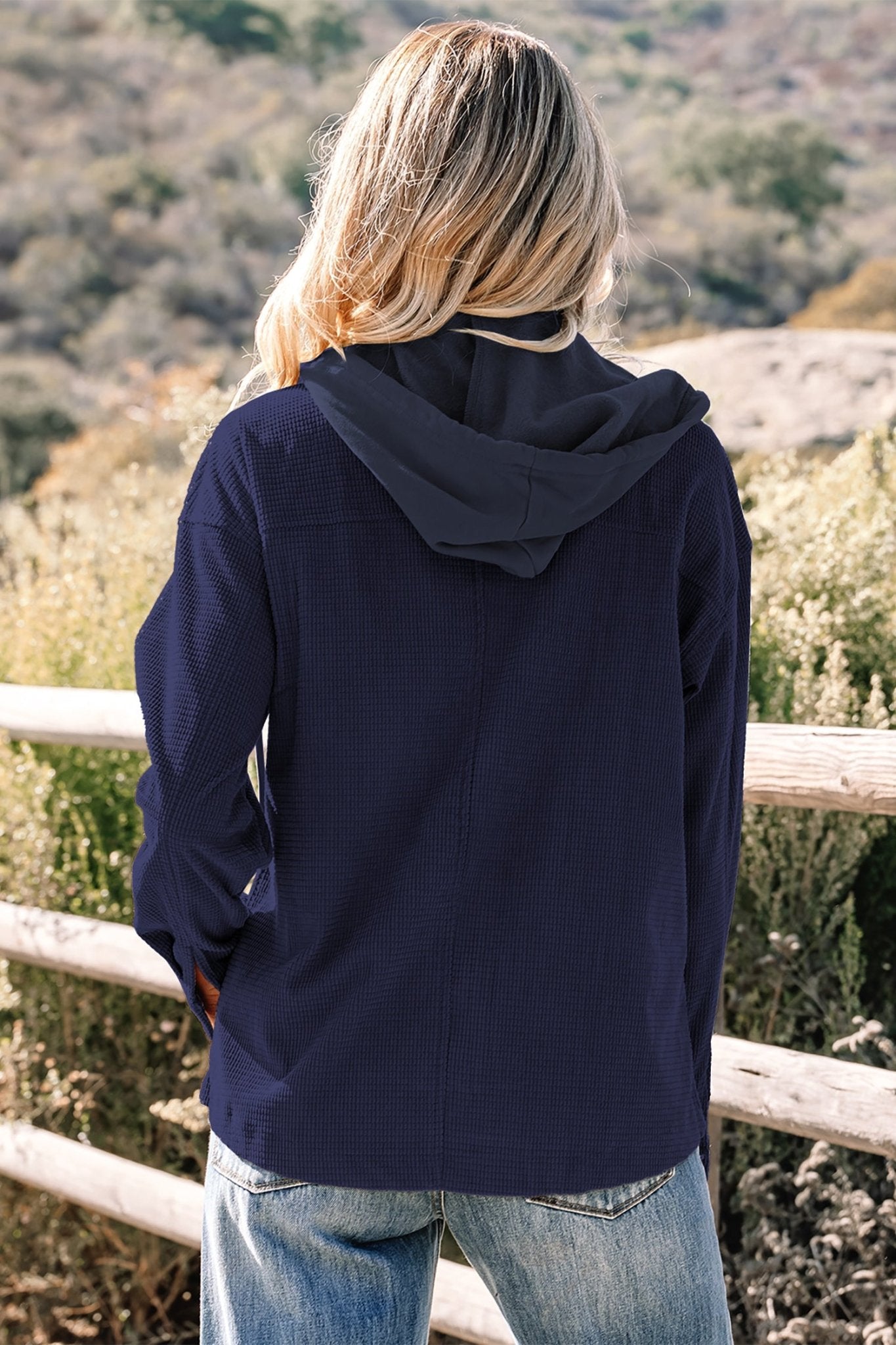 Person wearing a navy blue hoodie standing outdoors with a scenic background