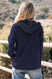Person wearing a navy blue hoodie standing outdoors with a scenic background